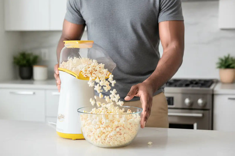 Person pouring popcorn from one of the best air popcorn poppers into a bowl in a kitchen.