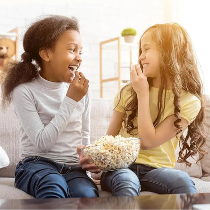 Two young girls enjoying popcorn together on a couch.