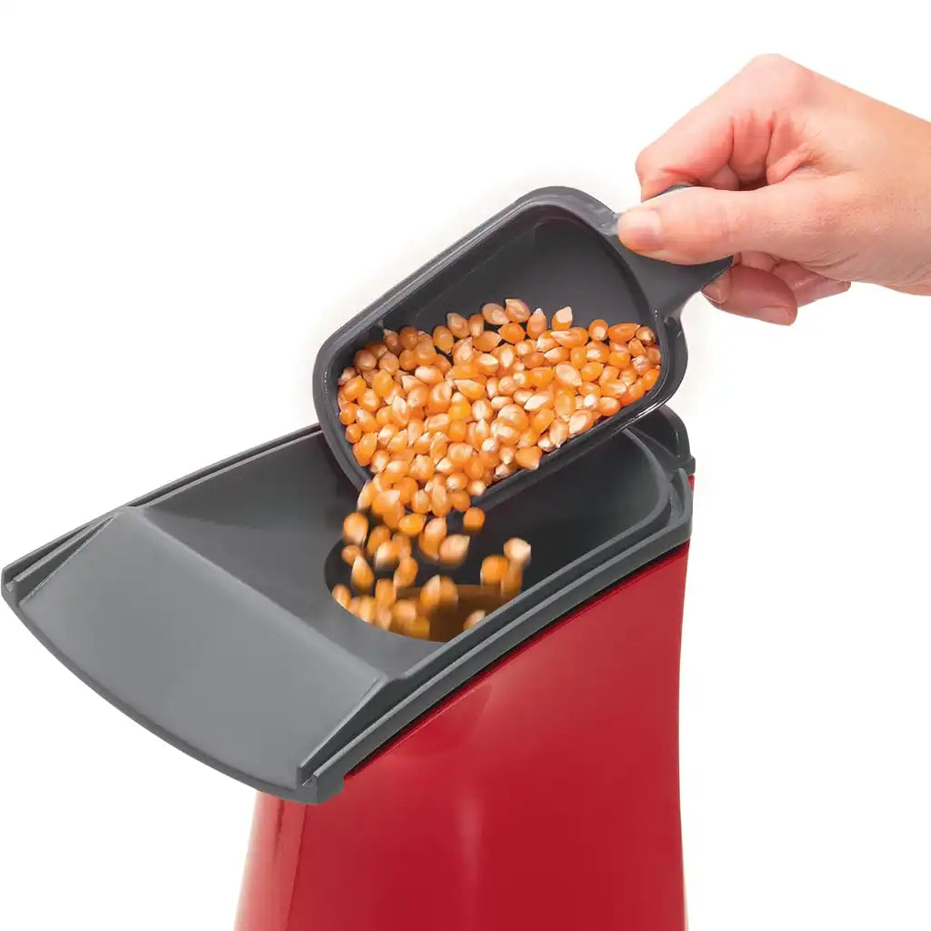 Hand pouring popcorn kernels into a red and gray air pop popcorn popper.