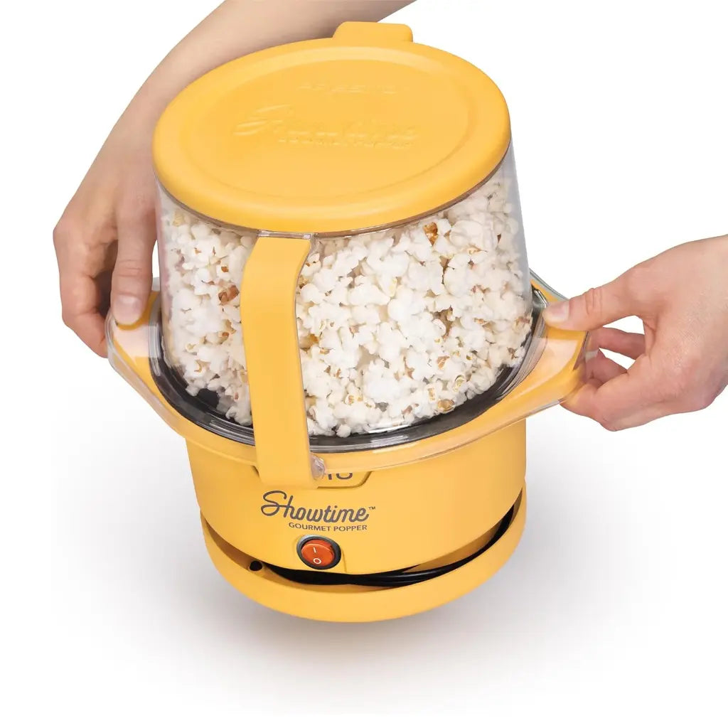 Electric popcorn popper with popped popcorn inside, held by two hands.