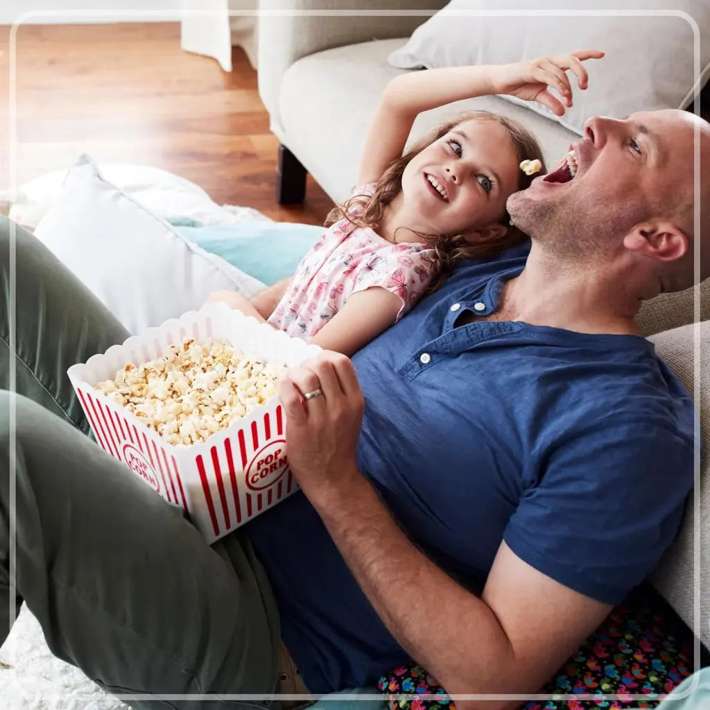Man and young girl enjoying popcorn together on a couch.