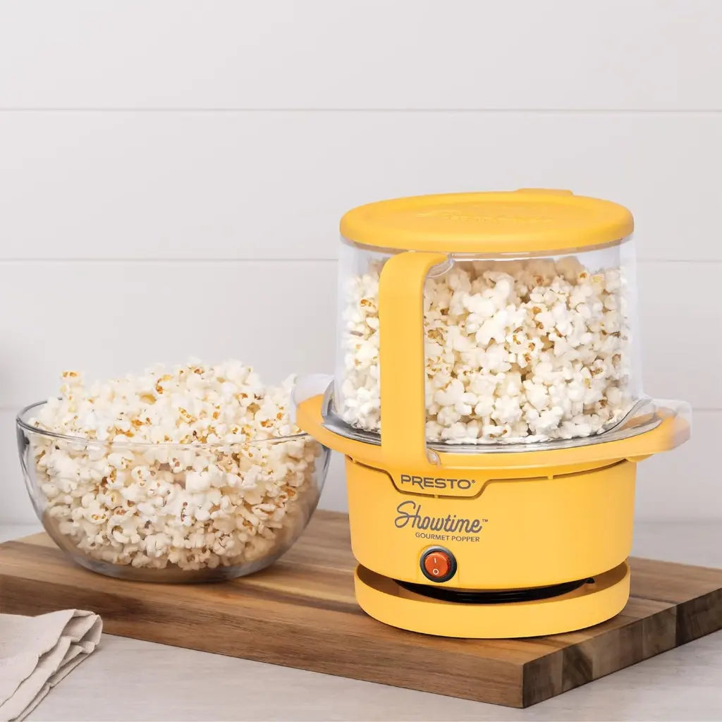 Oil popcorn popper with popped popcorn and a bowl of popcorn on a wooden board.