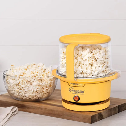 Oil popcorn popper with popped popcorn and a bowl of popcorn on a wooden board.