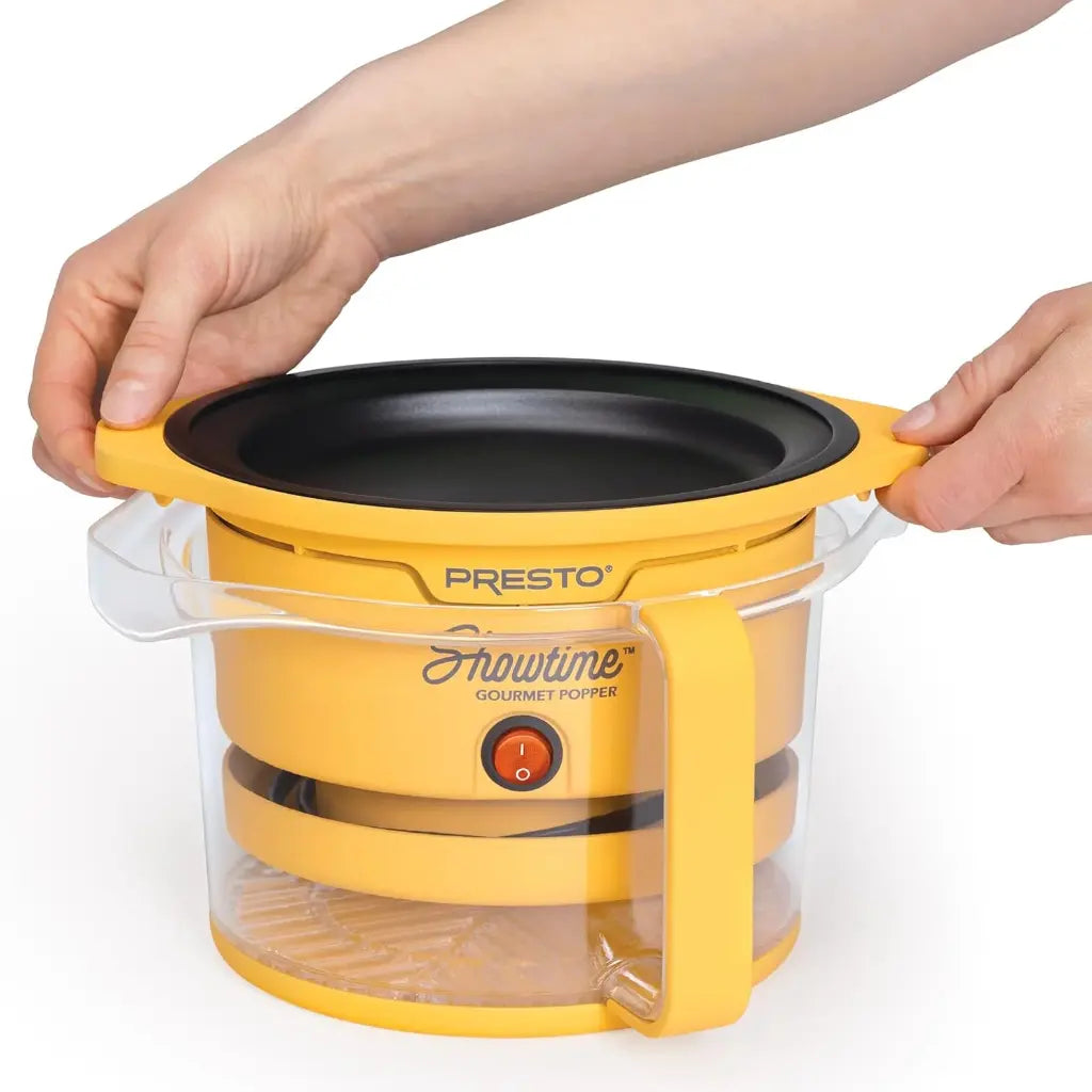 Oil popcorn popper with clear lid held by a hand.