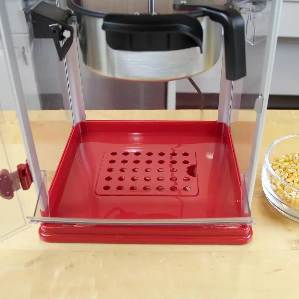Popcorn popper machine with a red base on a wooden surface.