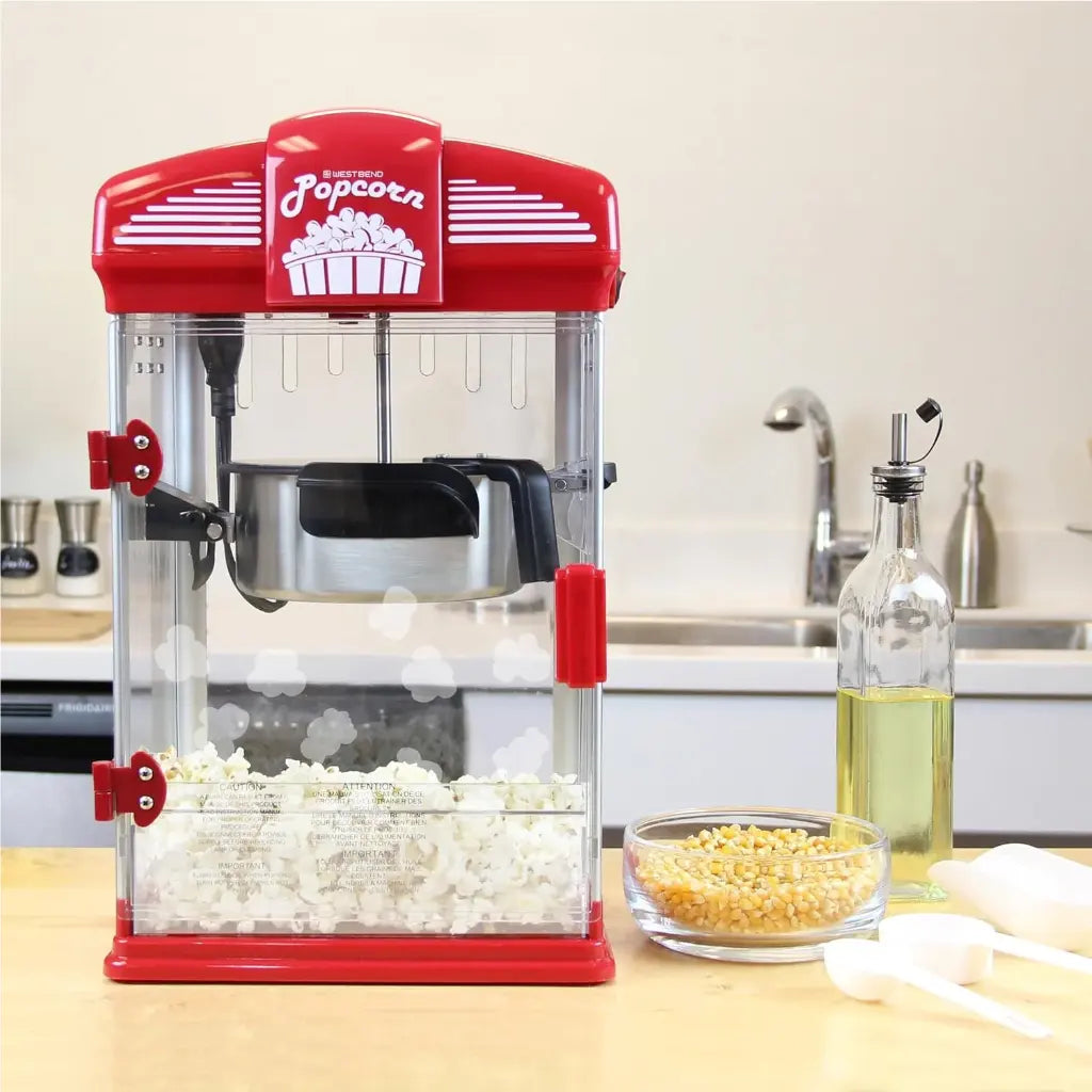 Popcorn popper machine on a kitchen counter with popped popcorn and kernels.